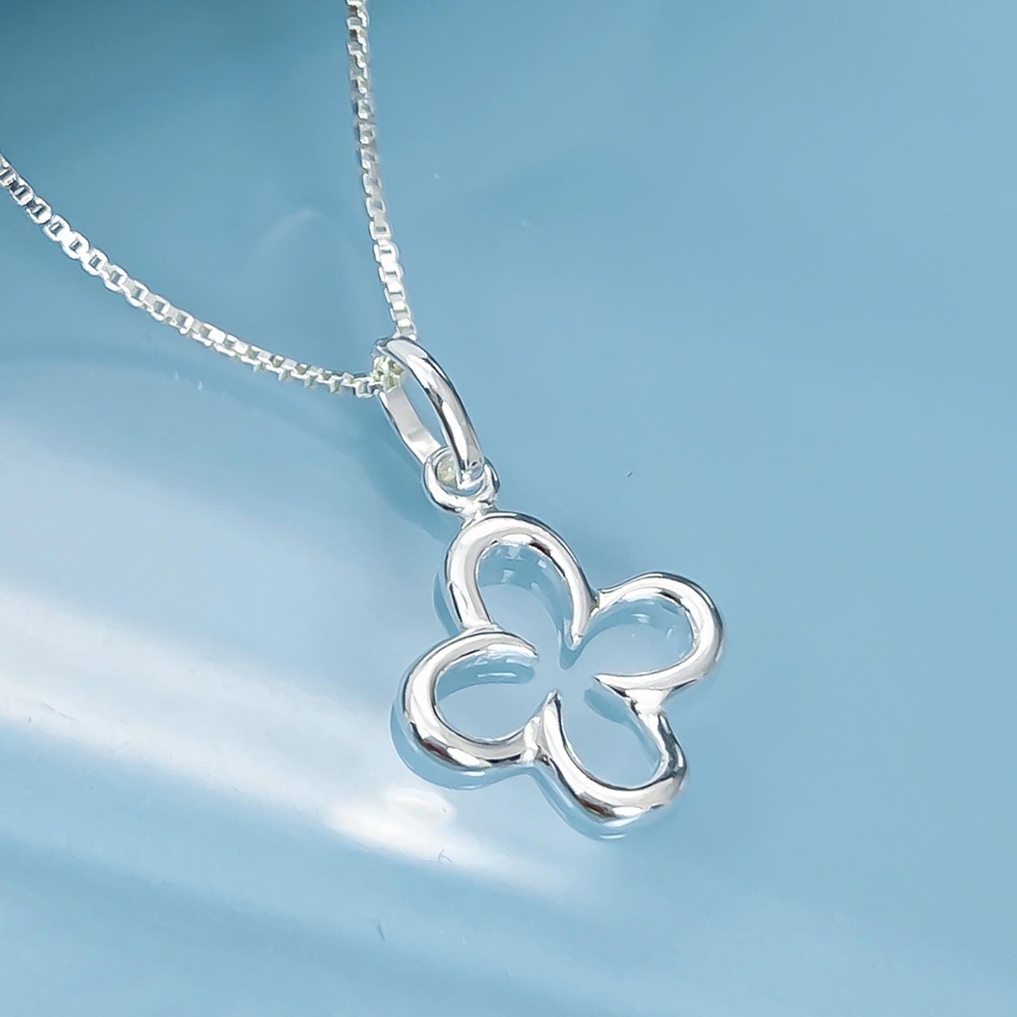 A silver flower pendant necklace with a chain is displayed against a blue background.