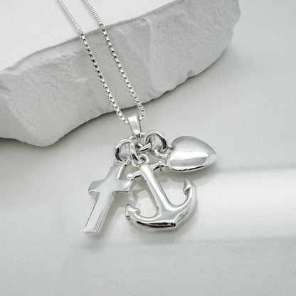 A silver necklace with a pendant featuring a cross, an anchor, and a heart charm.