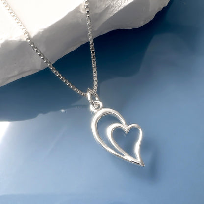 A silver heart-shaped pendant necklace with a chain is displayed against a blue background.