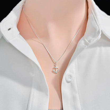 A silver necklace with a small anchor pendant is worn around a person's neck, who is wearing a white collared shirt.
