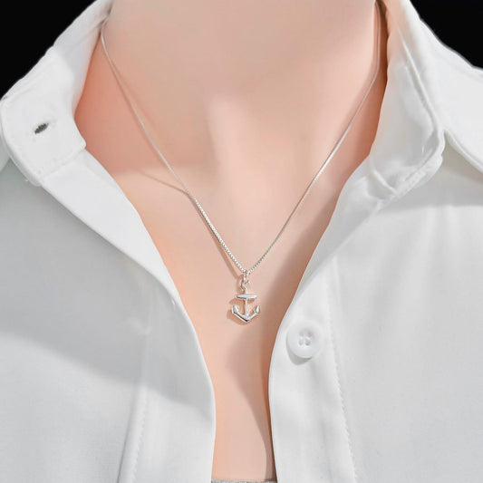 A silver necklace with a small anchor pendant is worn around a person's neck, who is wearing a white collared shirt.