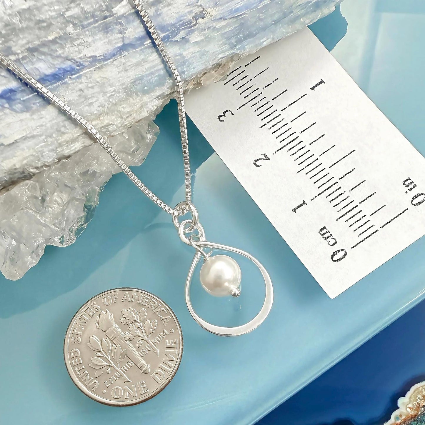 a silver necklace with a pearl pendant, placed next to a United States one dollar coin.