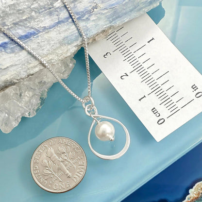a silver necklace with a pearl pendant, placed next to a United States one dollar coin.