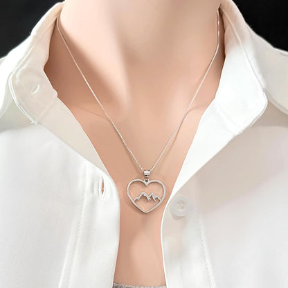 A silver necklace with a heart-shaped pendant featuring mountain peaks.