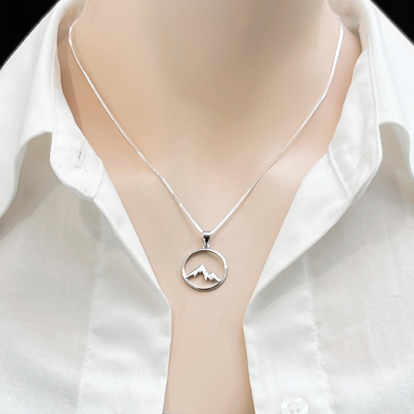 A silver necklace with a pendant featuring a mountain silhouette.