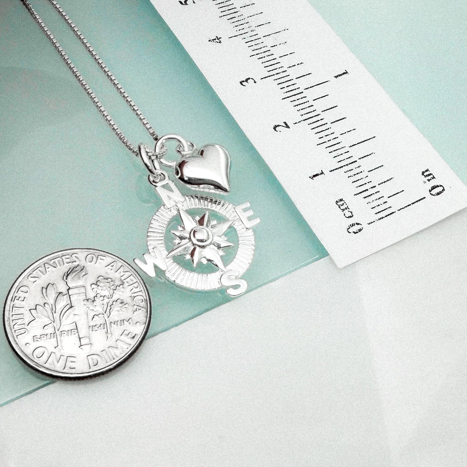 a silver compass pendant and a United States one-dollar coin, both placed on a light blue surface.