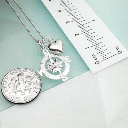 a silver compass pendant and a United States one-dollar coin, both placed on a light blue surface.