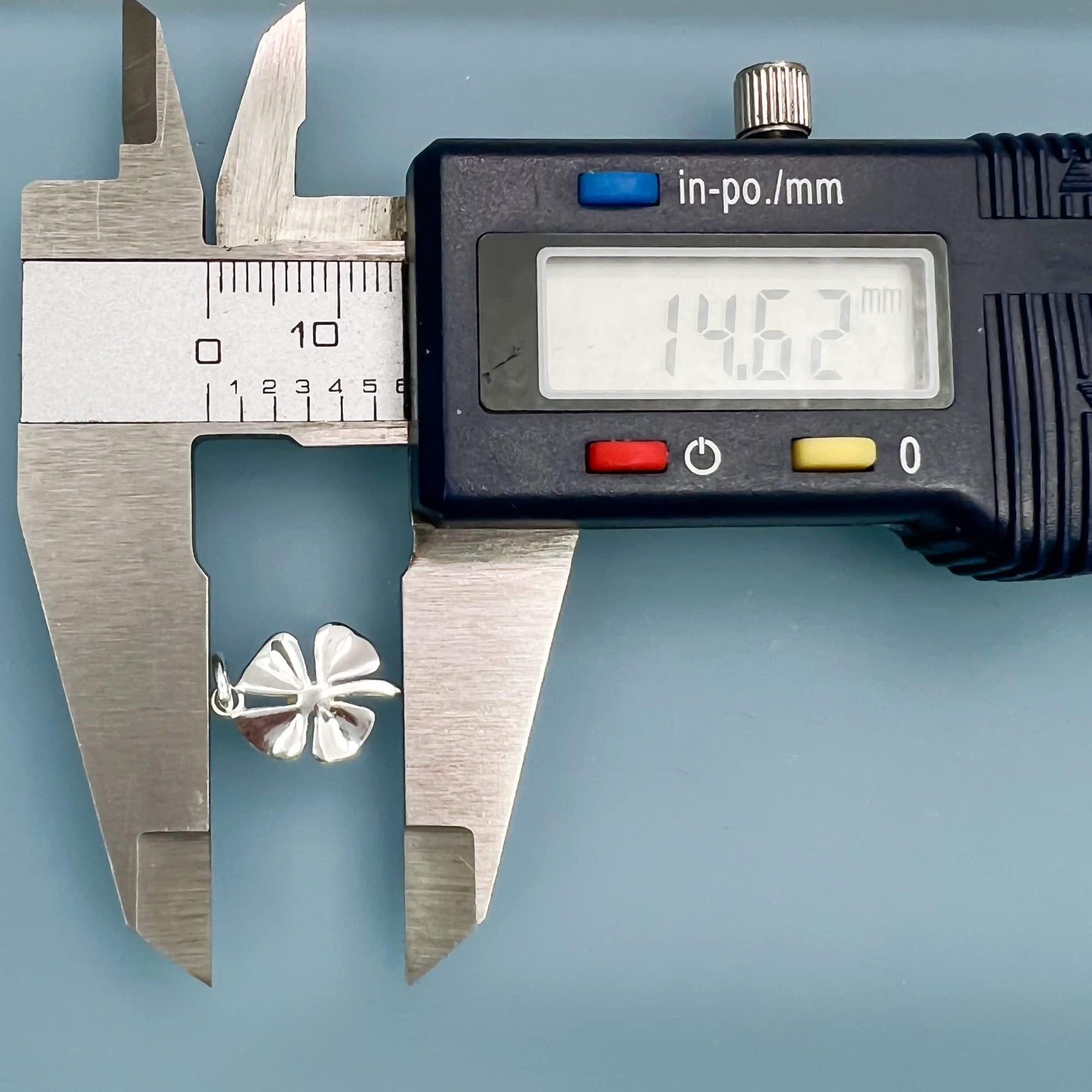 A digital caliper is being used to measure the size of a silver flower charm.