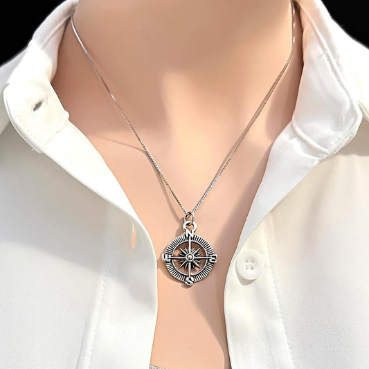 A silver compass pendant is worn on a necklace around a person's neck.