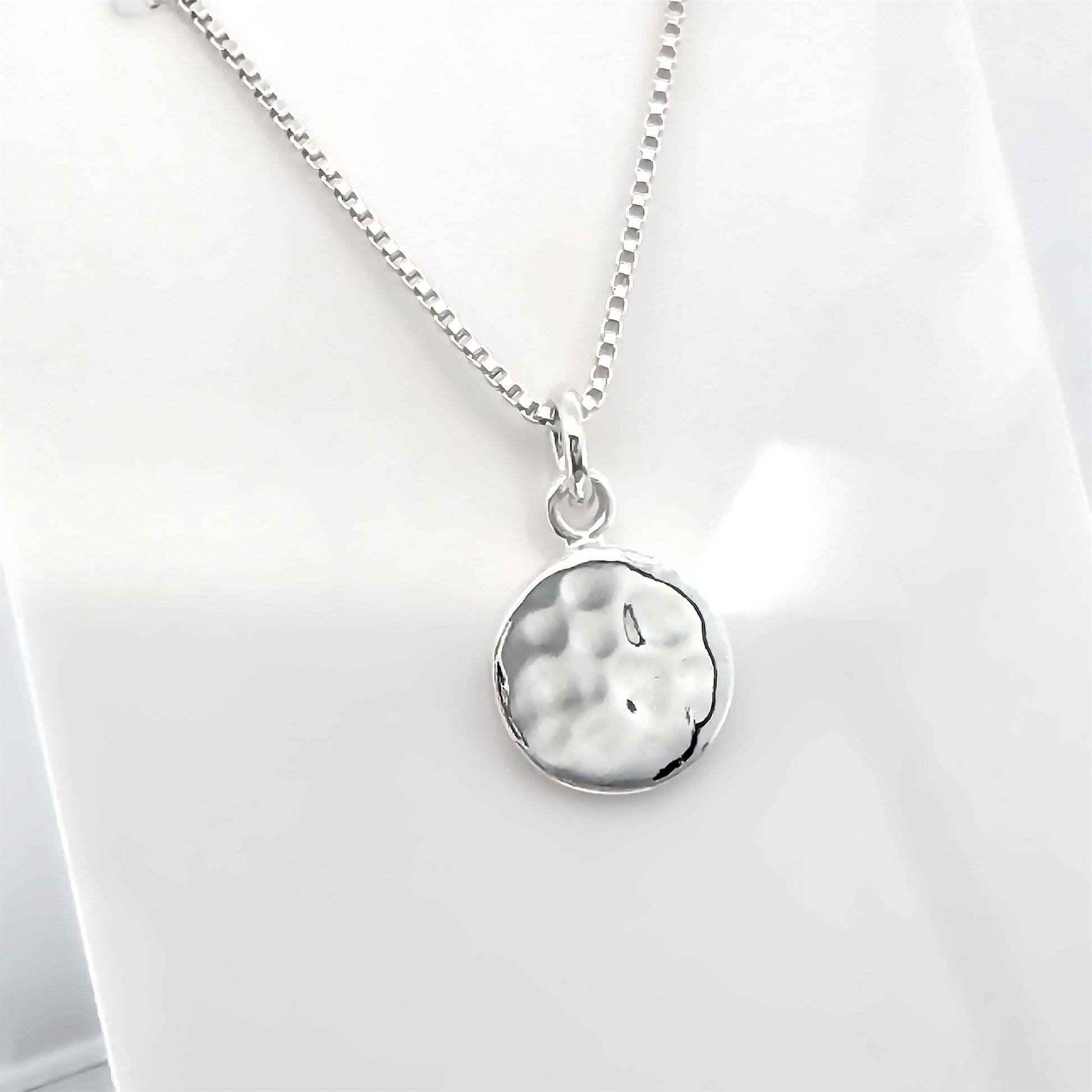A silver necklace with a round pendant is shown against a white background.