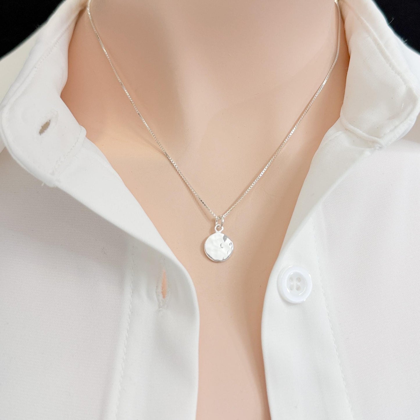 A close-up view of a person wearing a white collared shirt and a silver necklace with a small circular pendant.