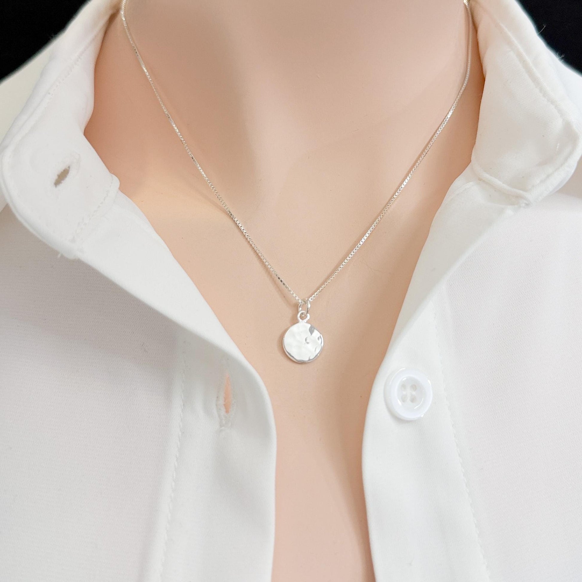 A close-up view of a person wearing a white collared shirt and a silver necklace with a small circular pendant.