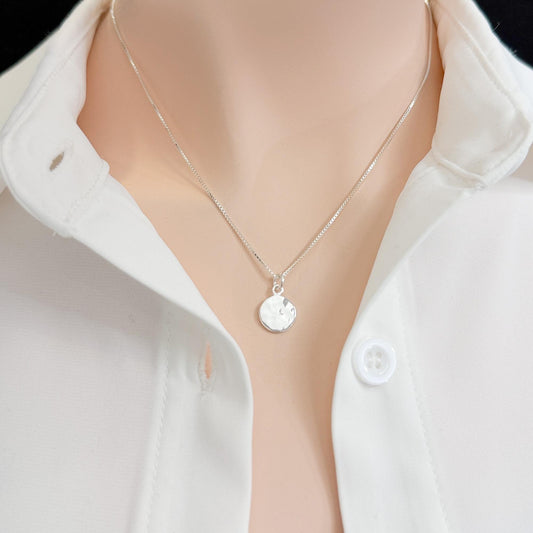 A close-up view of a person wearing a white collared shirt and a silver necklace with a small circular pendant.
