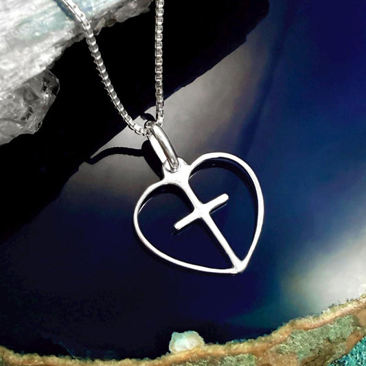A silver heart-shaped pendant with a cross is displayed on a blue and green background.