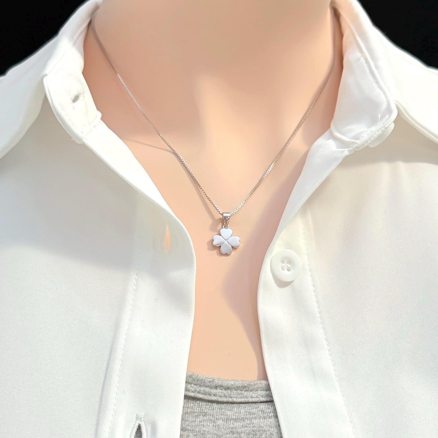 A close-up view of a person wearing a white collared shirt and a silver necklace with a small flower pendant.