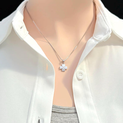 A close-up view of a person wearing a white collared shirt and a silver necklace with a small flower pendant.