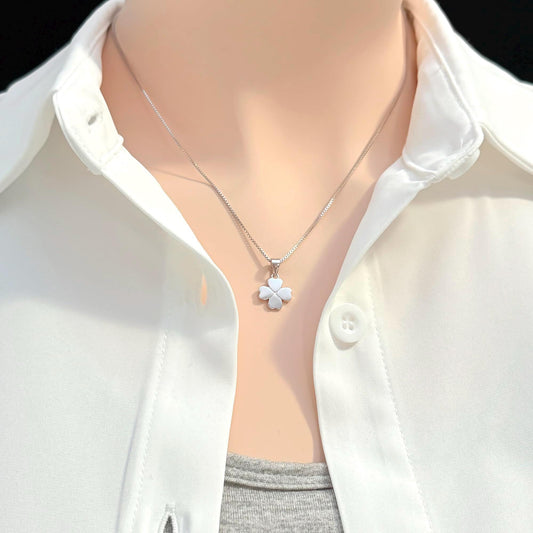 A close-up view of a person wearing a white collared shirt and a silver necklace with a small flower pendant.