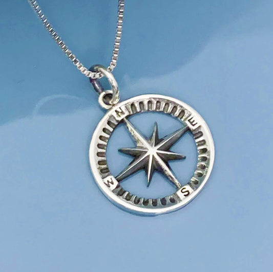 A silver compass pendant with a star at the center, hanging from a chain against a blue background.
