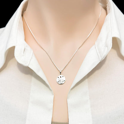 A silver necklace with a round pendant is displayed on a mannequin wearing a white collared shirt.