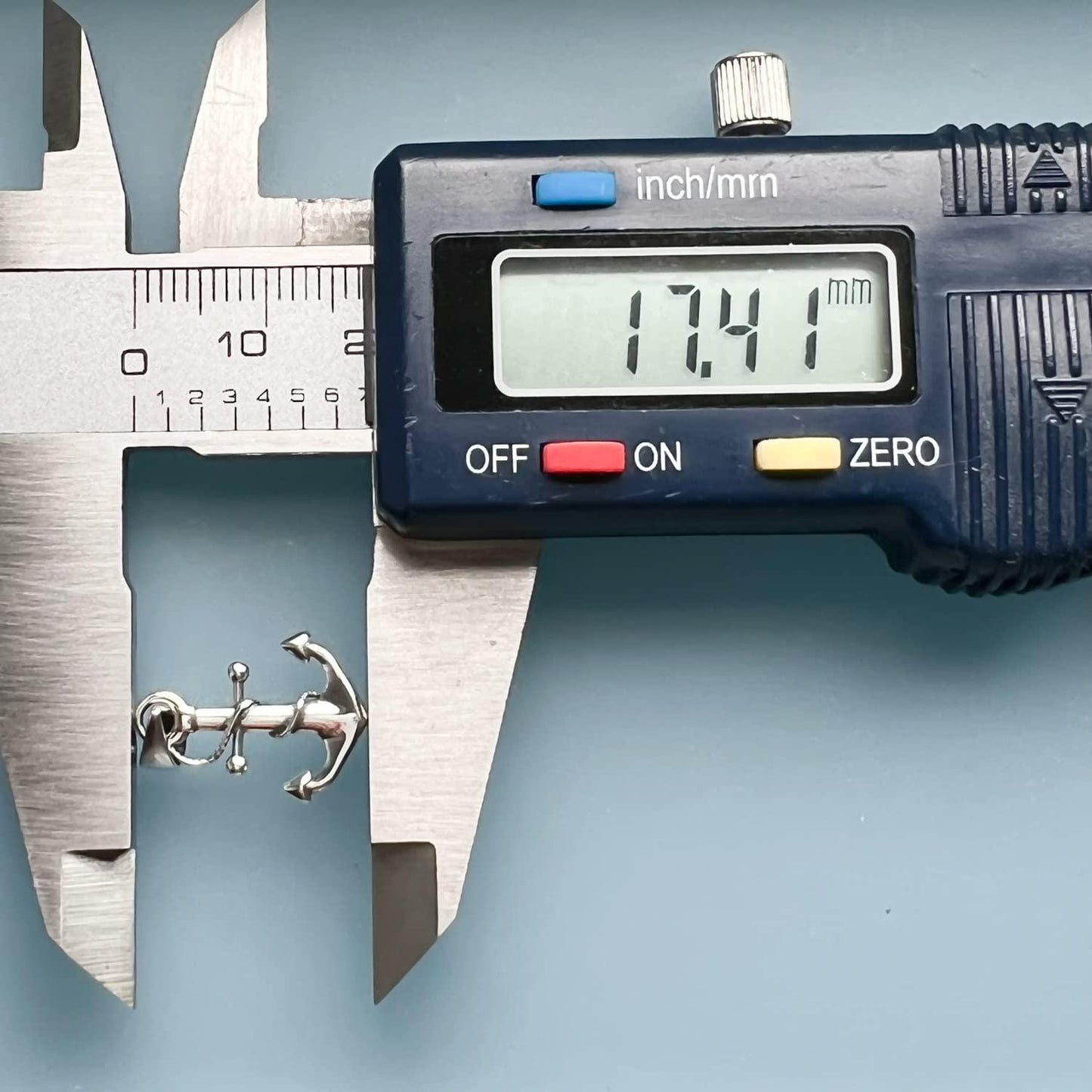 A digital caliper is being used to measure the size of a small object, which appears to be an anchor. The caliper is displaying the size of the object as 17.41 millimeters.