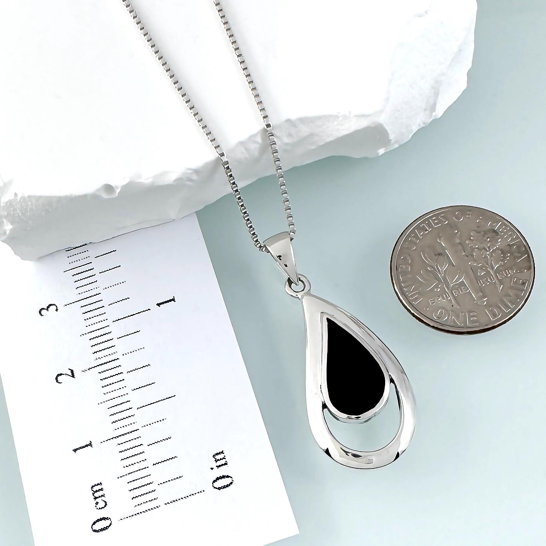 a silver necklace with a pendant, a ruler for scale, and a coin for size comparison.