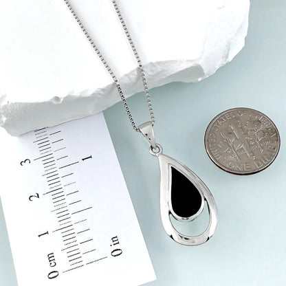 a silver necklace with a pendant, a ruler for scale, and a coin for size comparison.