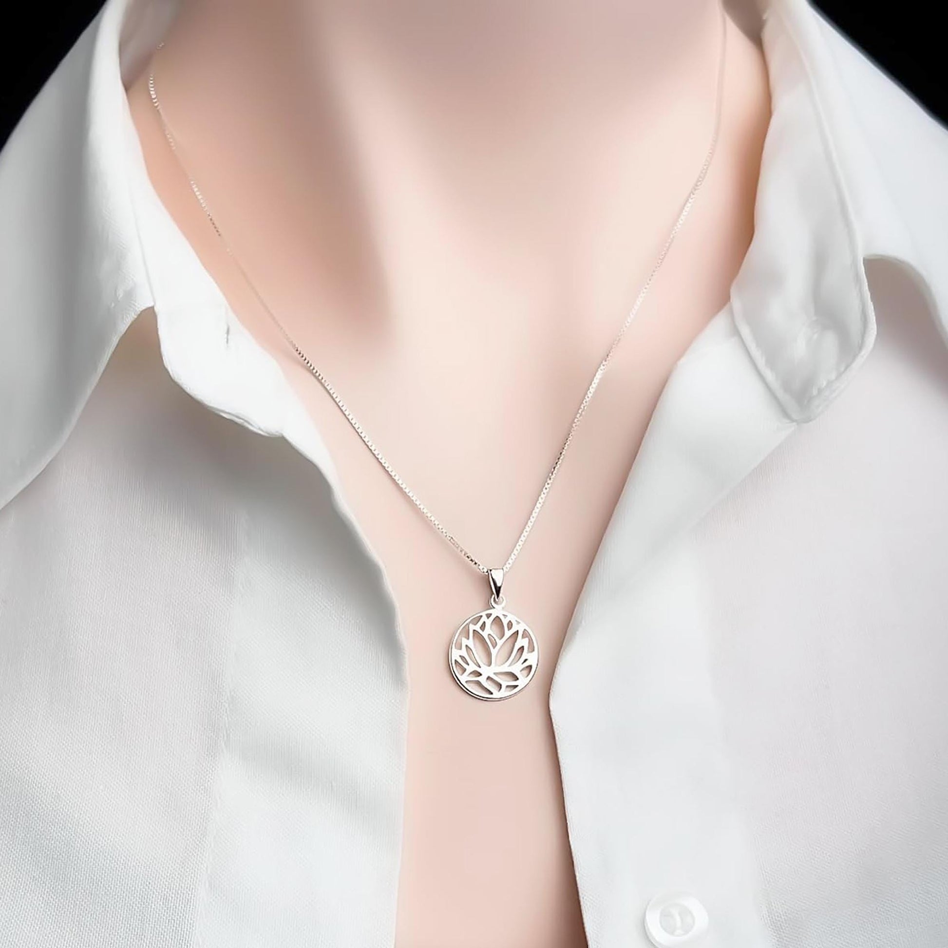 A silver necklace with a pendant featuring a floral design is worn around a person's neck.