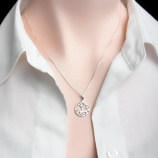A silver necklace with a pendant featuring a floral design is worn around a person's neck.