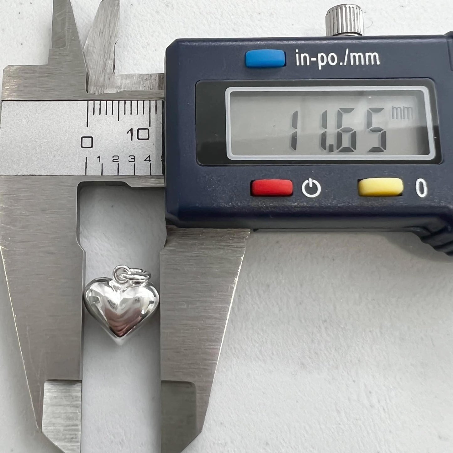 A silver heart-shaped charm is being measured with a caliper, which displays the size as 1.65 millimeters.