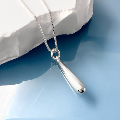 A silver necklace with a pendant is displayed against a blue background.