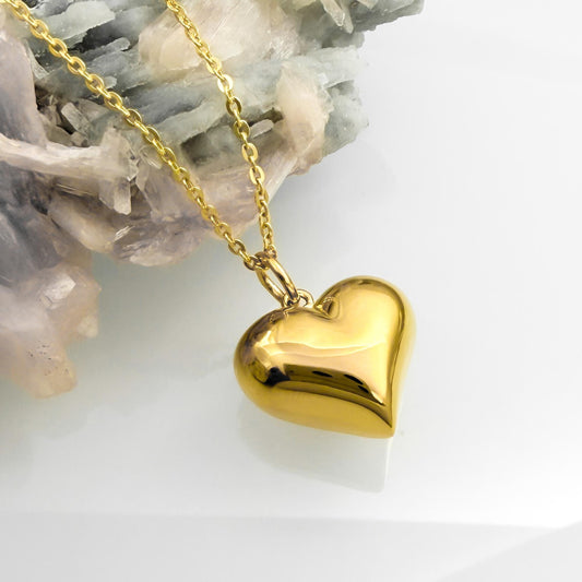A shiny gold heart-shaped pendant necklace is displayed against a white background.