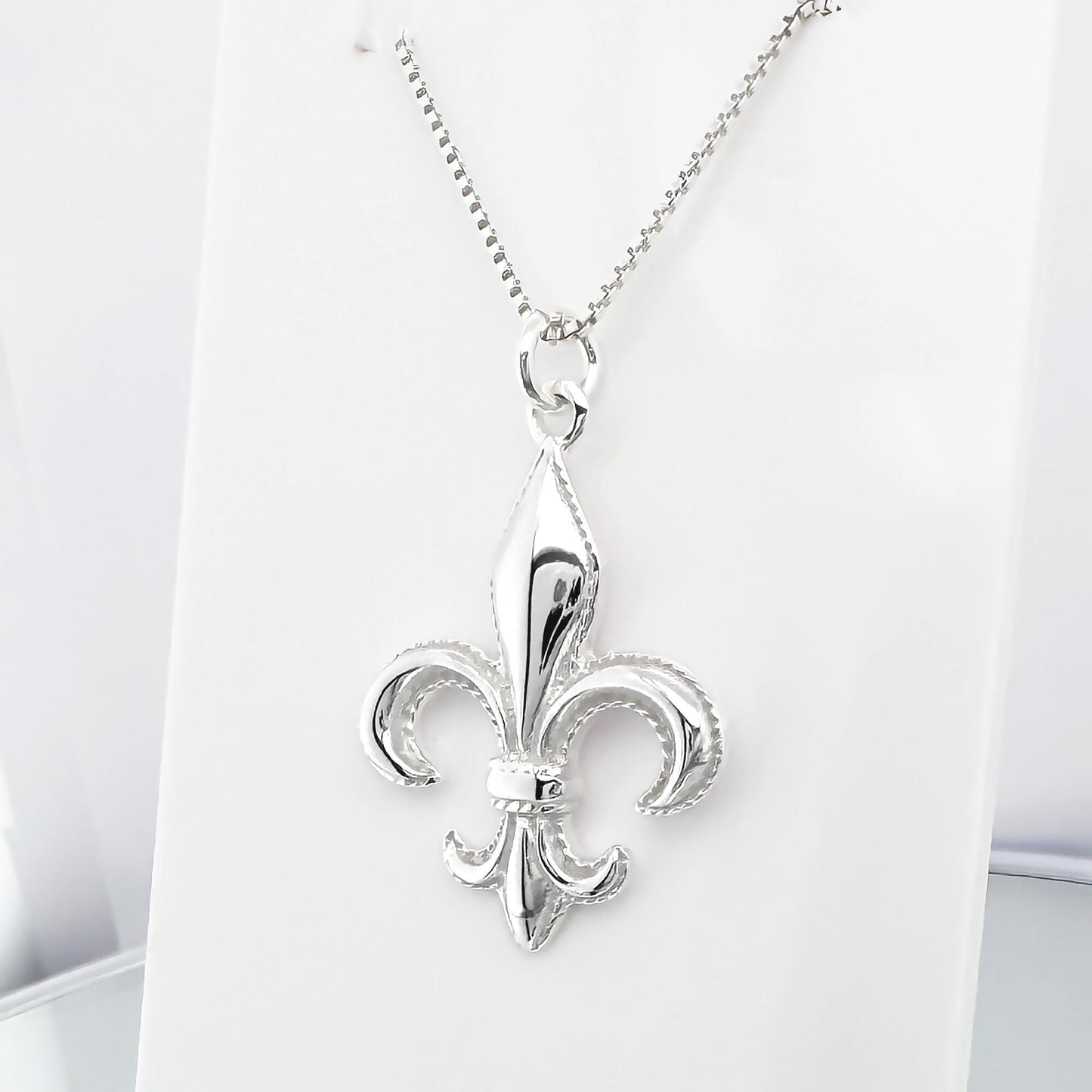 A silver-colored pendant necklace with a fleur-de-lis design.