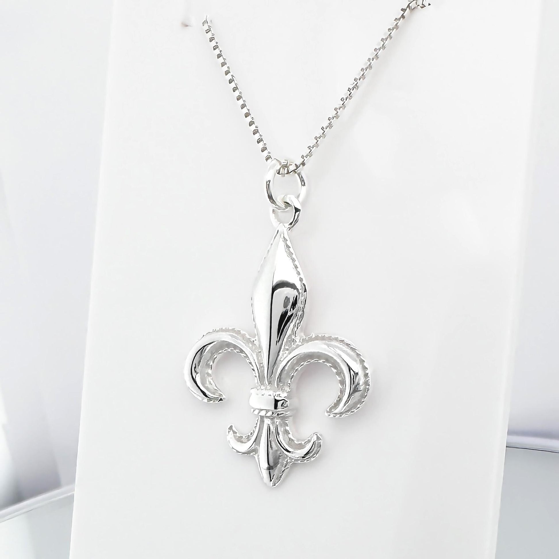 A silver-colored pendant necklace with a fleur-de-lis design.