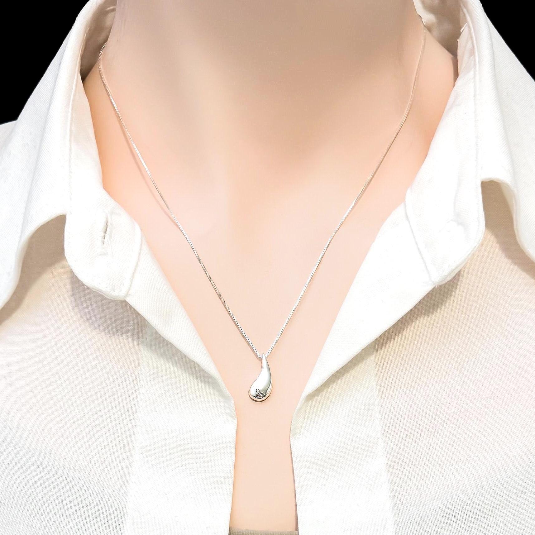 A close-up view of a mannequin wearing a white collared shirt and a silver necklace with a pendant.