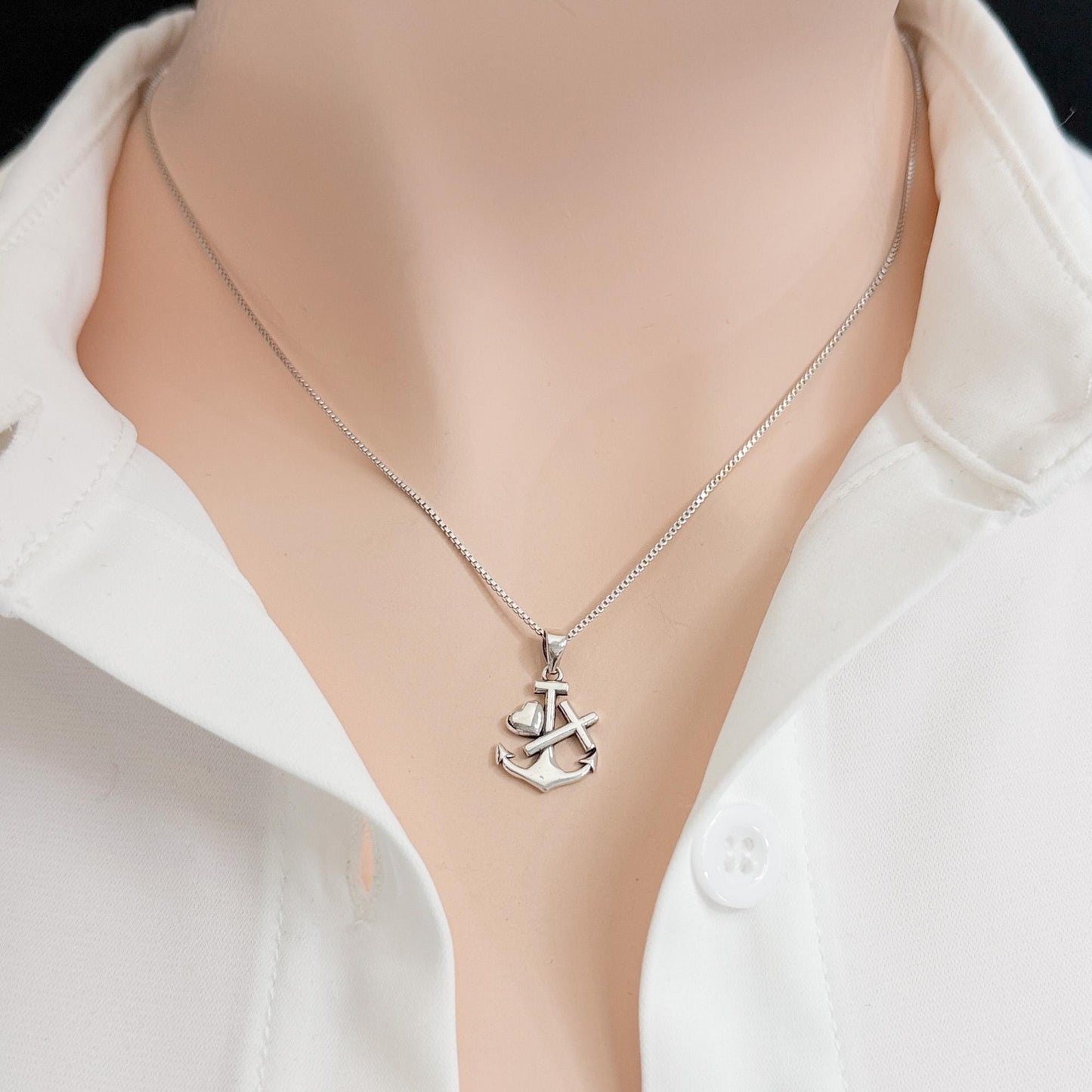 A silver necklace with a pendant featuring an anchor design is shown against a white shirt.