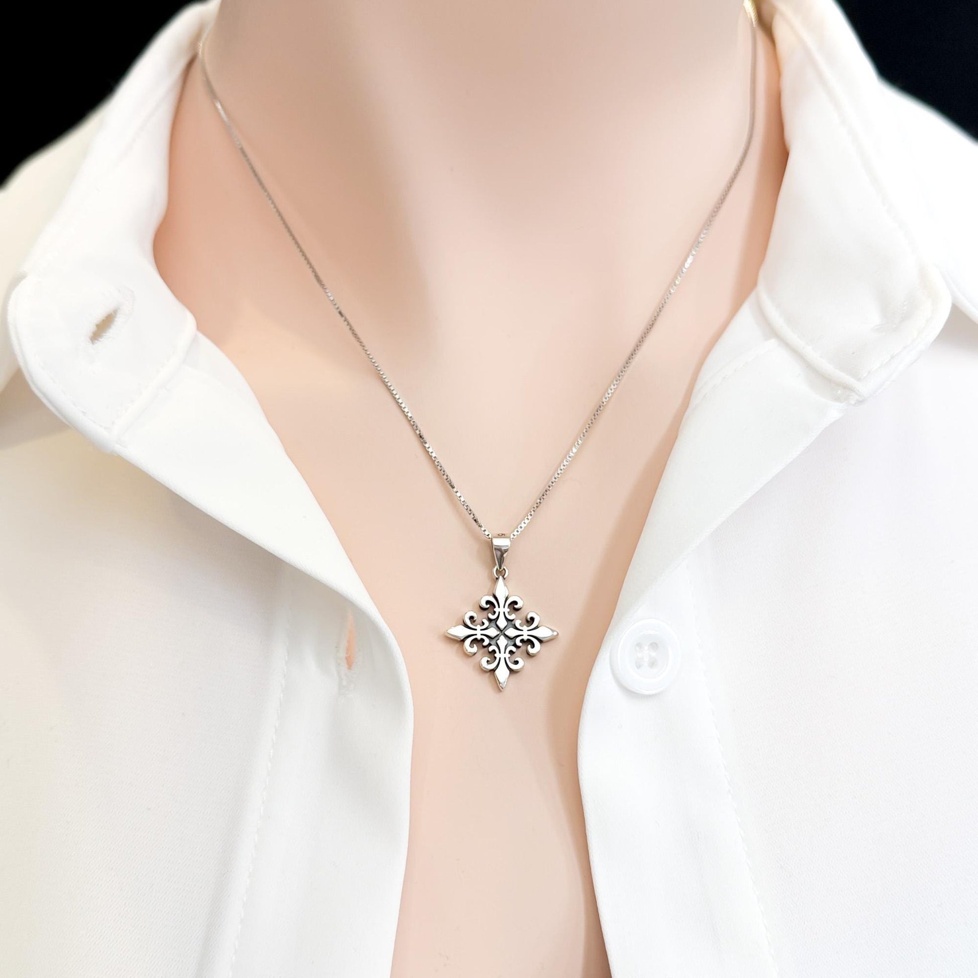 A silver necklace with a pendant is displayed on a person wearing a white collared shirt.