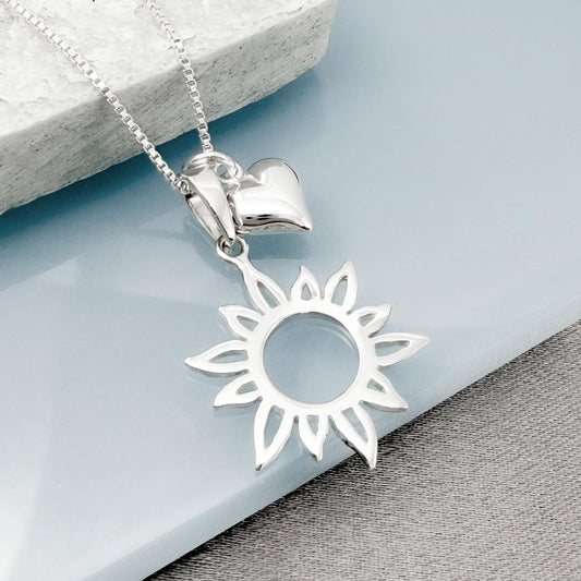A silver necklace with a pendant featuring a sun design and a heart shape.