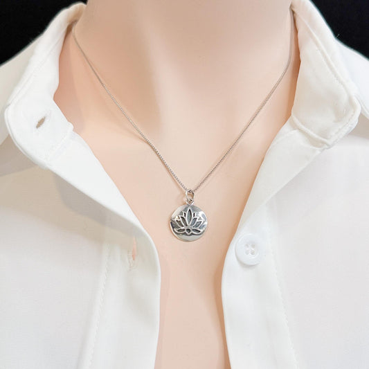 A silver necklace with a pendant featuring a lotus flower design is worn around a person's neck.