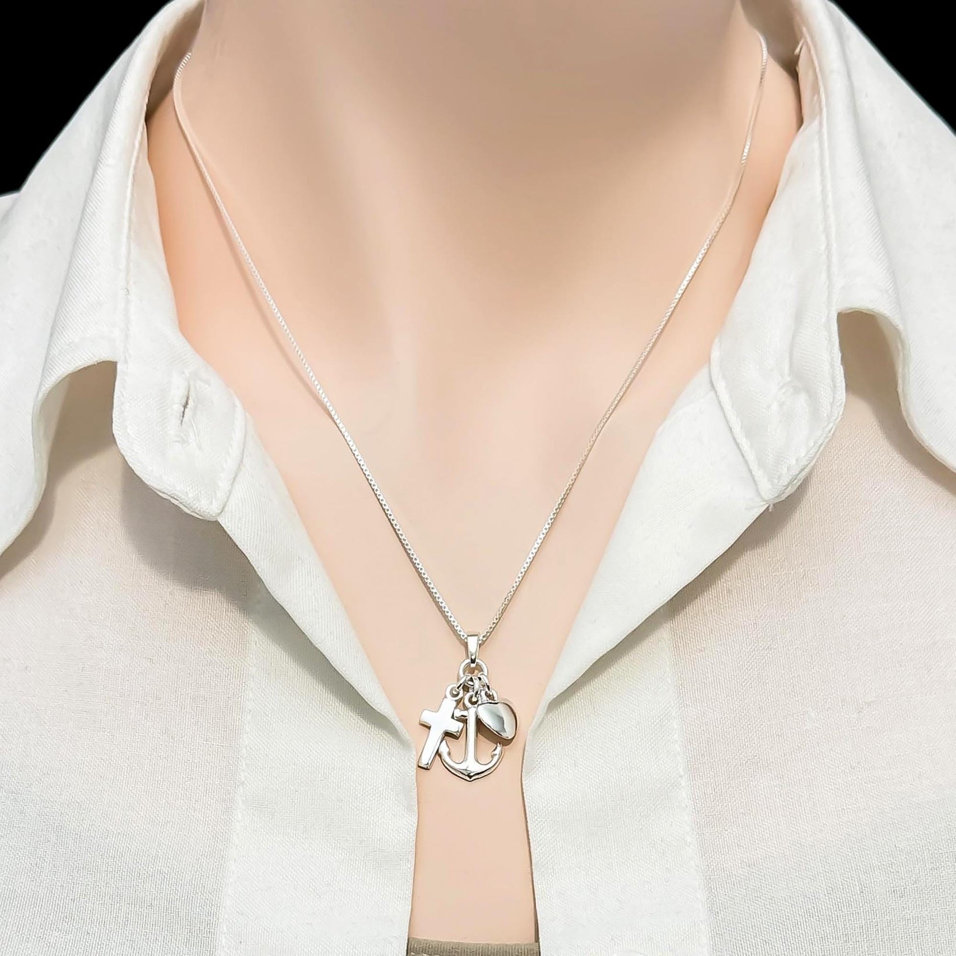 A silver necklace with a cross pendant and an anchor charm is displayed on a mannequin's neck.