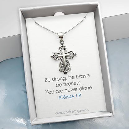 a silver cross pendant necklace displayed in a white box with a Bible verse printed on the box.