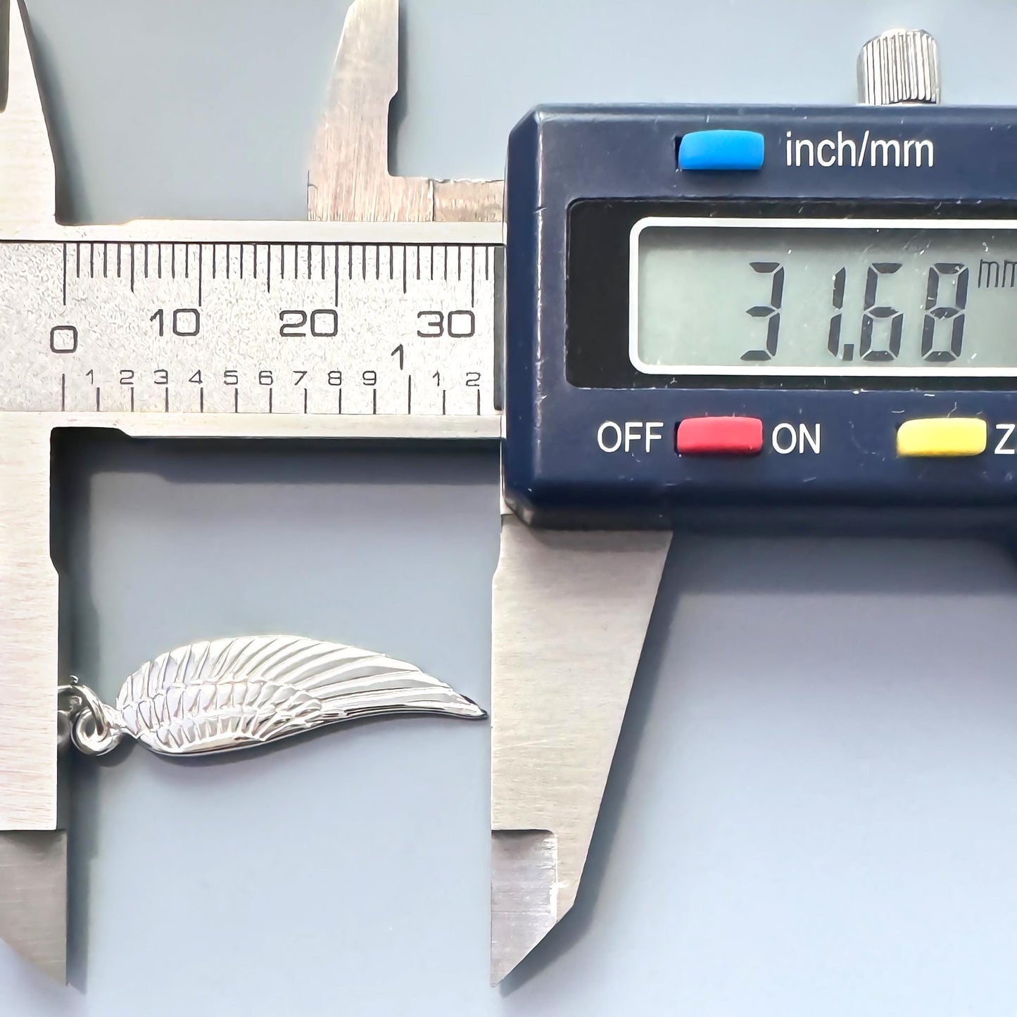 A digital caliper is being used to measure the size of a silver feather-shaped object, which appears to be a necklace charm.