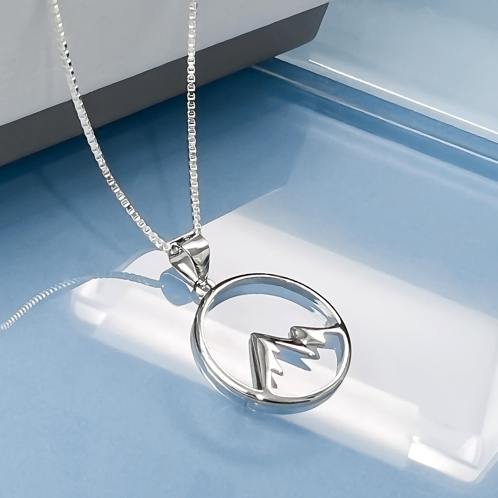 A silver necklace with a pendant featuring a mountain silhouette design.