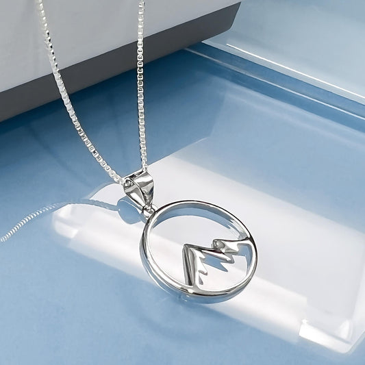 A silver necklace with a pendant featuring a mountain silhouette design.