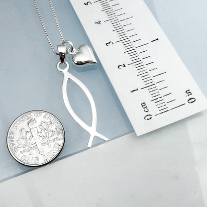 a silver necklace with a pendant, a silver coin, and a ruler placed on a light blue surface.