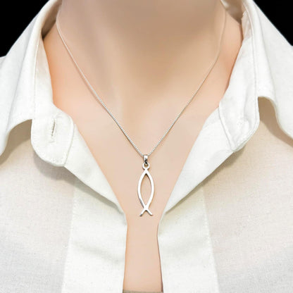 A silver necklace with a pendant is worn around a person's neck, who is wearing a white collared shirt.