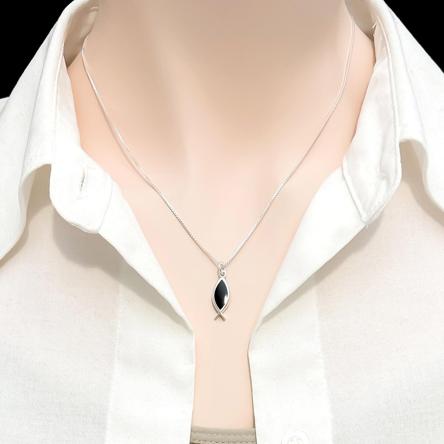 A silver necklace with a pendant is worn around a mannequin's neck, set against a white collared shirt.