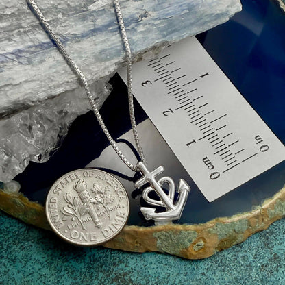 a silver necklace with a pendant and a United States one-dollar coin placed on a blue and green surface.