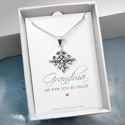 A silver necklace with a pendant is displayed in a white box, accompanied by a card that reads "Grandma we love you so much!"