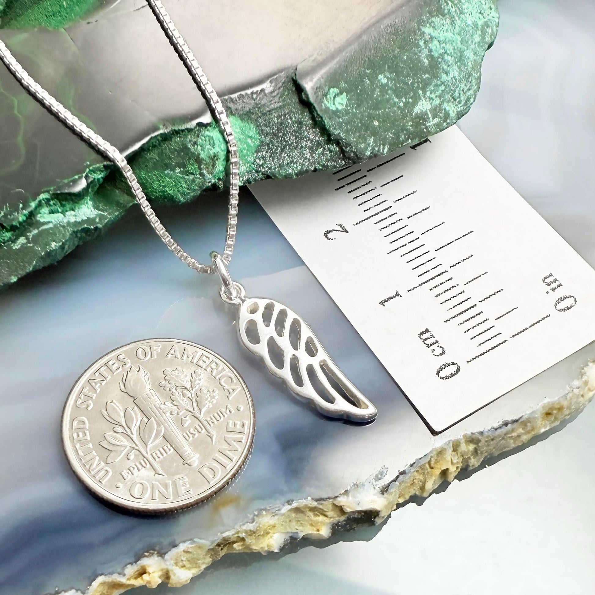 a silver necklace with a pendant, a silver coin, and a ruler placed on a green and white surface.