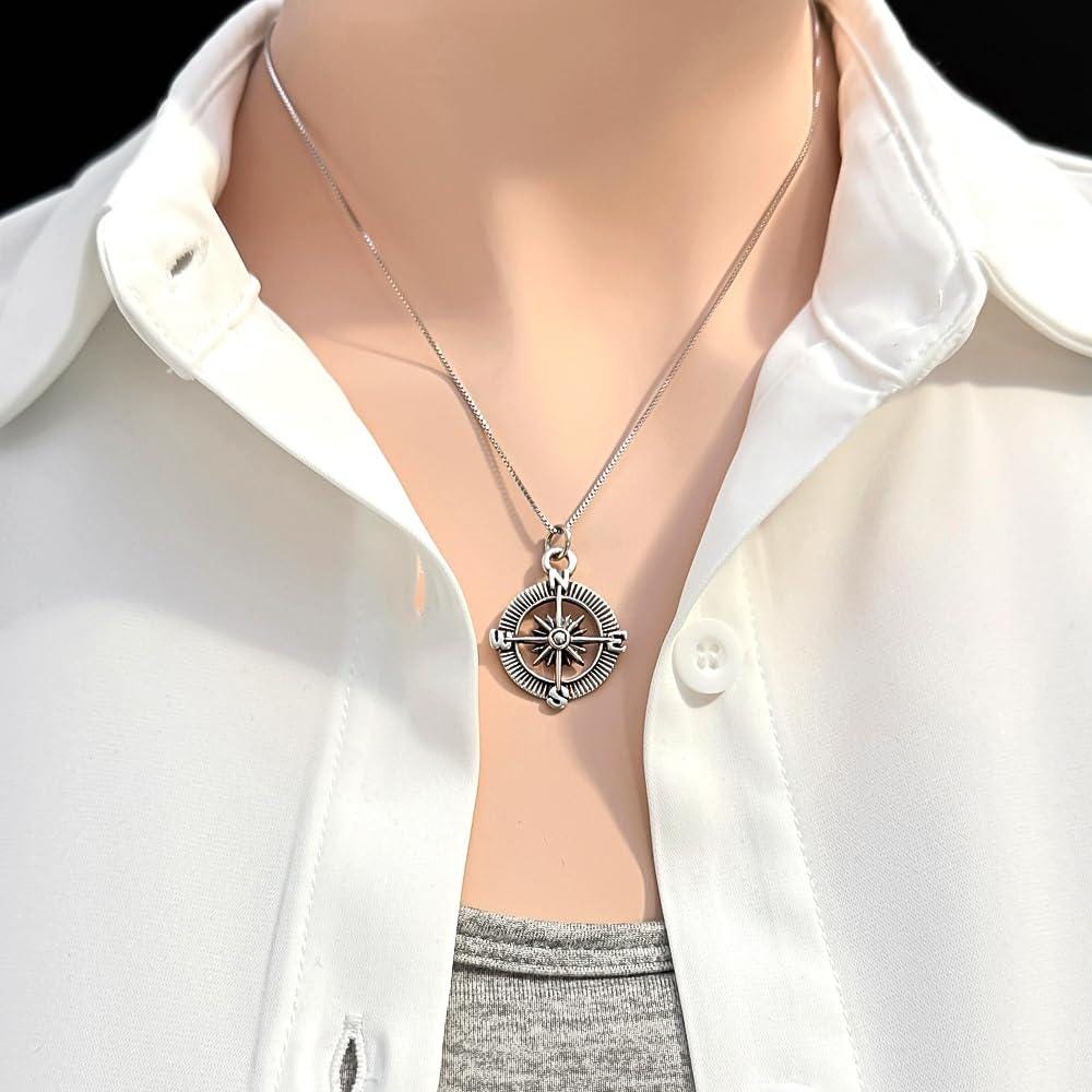 A silver compass pendant is worn on a white shirt, with the focus on the pendant and the collar of the shirt.